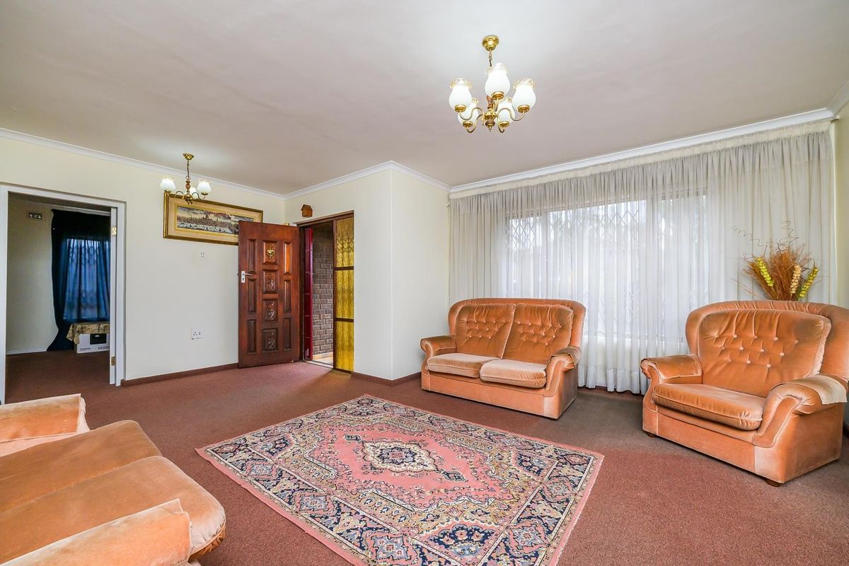 A spacious living room featuring classic coving, a central chandelier, and a solid timber entrance door with security gate access.