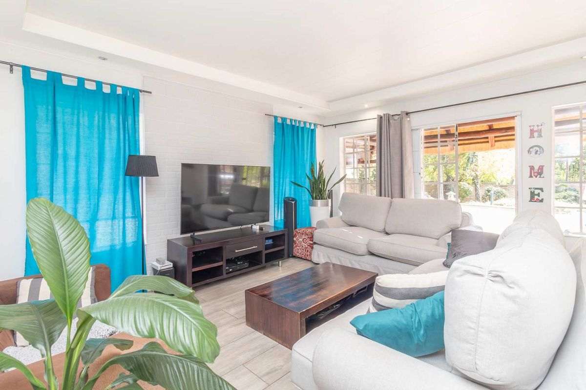 A bright living room featuring painted brick walls, tiled flooring, and large windows providing natural light and access to the outdoor patio area.