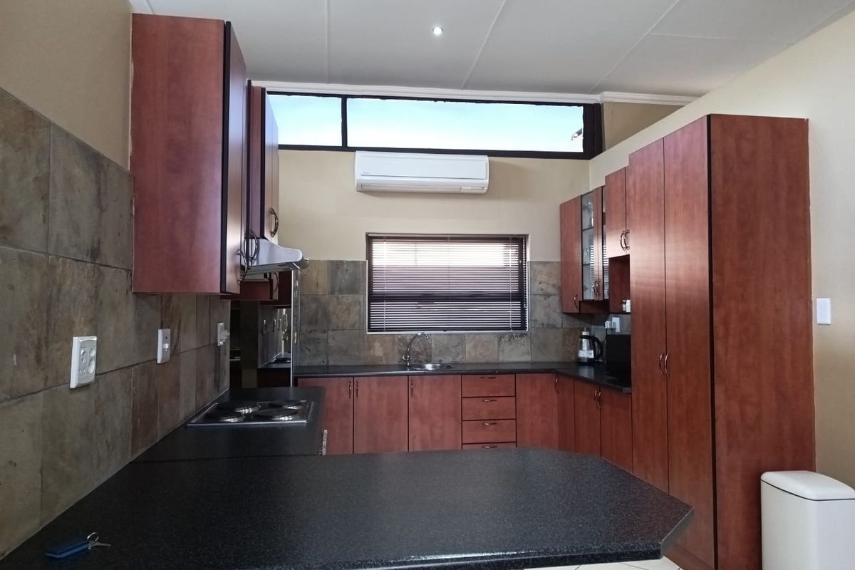 A functional kitchen featuring dark wood cabinetry, black countertops, a built-in hob, and a wall-mounted air conditioning unit.