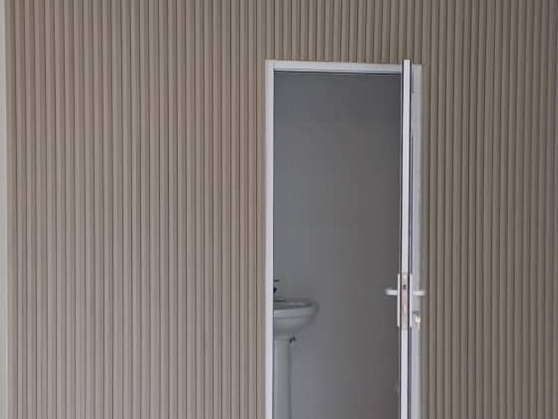A clean, modern hallway featuring decorative vertical wall paneling, tiled flooring, and a contemporary ceiling light fixture, leading to an adjacent bathroom.