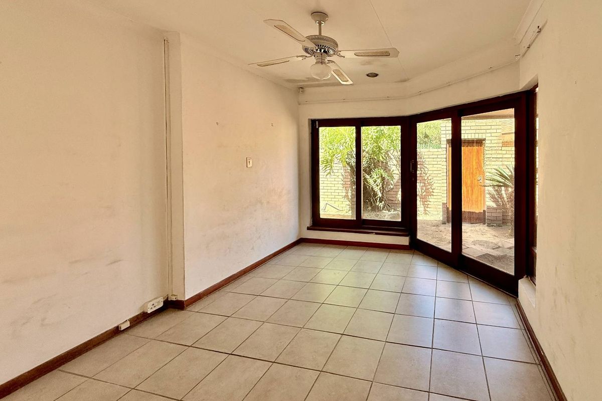 An empty living room featuring tiled flooring, a ceiling fan, and large sliding glass doors providing direct access to the rear garden area.