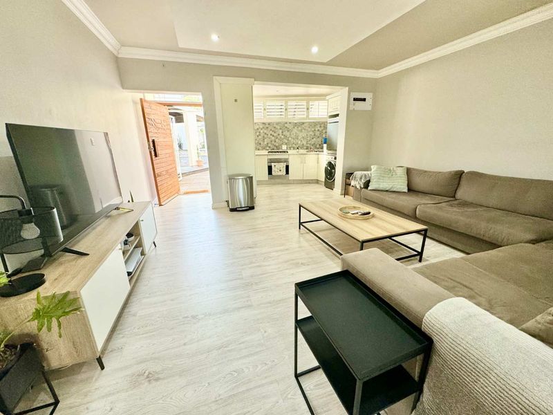 Open plan living area featuring light laminate flooring, recessed ceiling lighting, and a functional kitchen with built-in appliances and tiled backsplash.