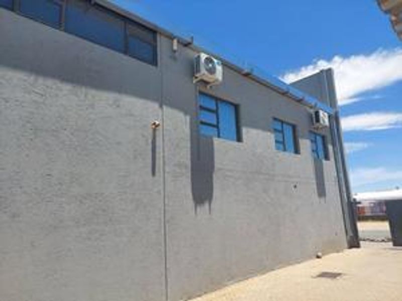 Exterior view of the industrial building featuring a textured grey facade, multiple aluminium windows, and wall-mounted air conditioning units.