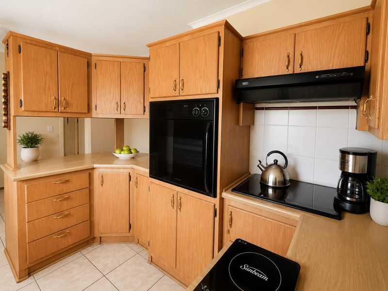 A functional kitchen featuring light wood-tone cabinetry, built-in oven, ceramic hob, and tiled splashback, offering a classic and practical layout.
