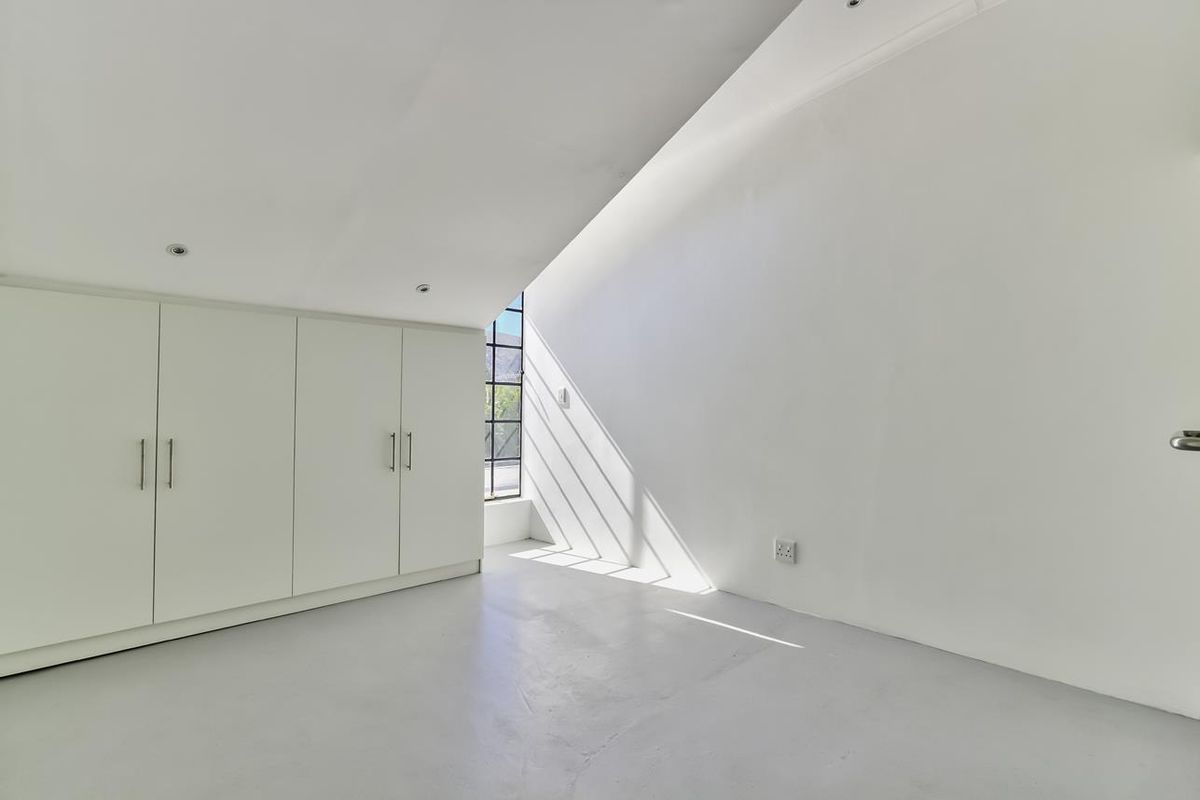 A bright, minimalist bedroom featuring built-in cabinetry, smooth flooring, and a large window that allows for ample natural light.