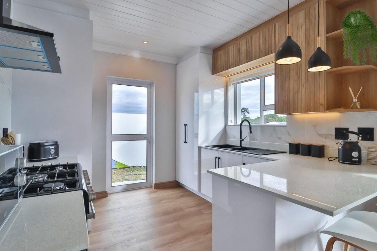 Modern kitchen featuring sleek white cabinetry, timber accents, stone countertops, a gas cooktop, and high-quality finishes with direct access to the exterior.