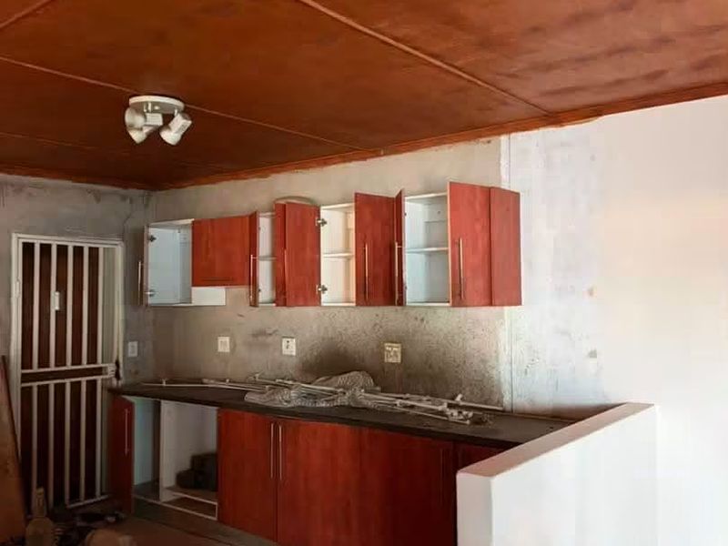 An unfinished kitchen area featuring wooden ceiling panels, built-in cabinetry, and tiled flooring, currently undergoing renovation or requiring completion.