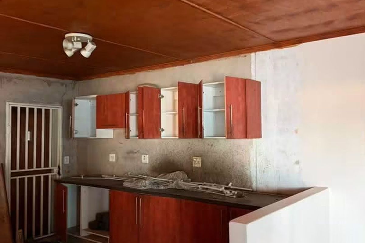An unfinished kitchen area featuring wooden ceiling panels, built-in cabinetry, and tiled flooring, currently undergoing renovation or requiring completion.