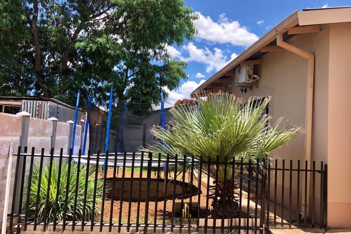 Rear exterior view of the property featuring a fenced garden area, concrete boundary wall, and external air conditioning unit.