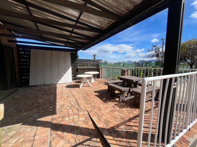 A covered outdoor patio area featuring stone paving, metal railings, and a corrugated roof, offering an open space for outdoor entertainment.