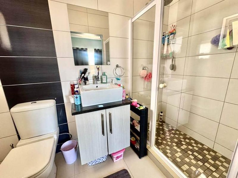 A functional bathroom featuring a vessel sink vanity, a glass-enclosed shower with mosaic floor tiles, and modern wall tiling.