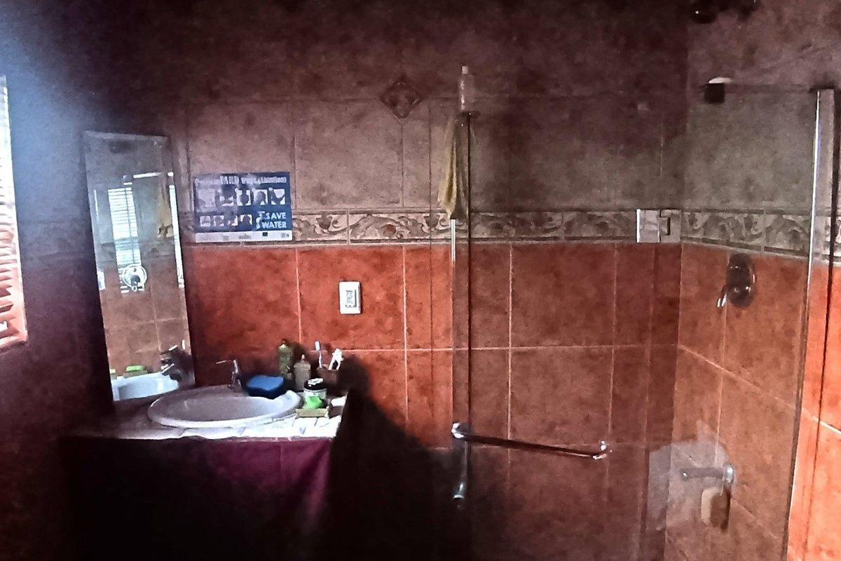 A dated bathroom featuring a vanity basin, glass shower enclosure, and full-height wall tiling with a decorative border.