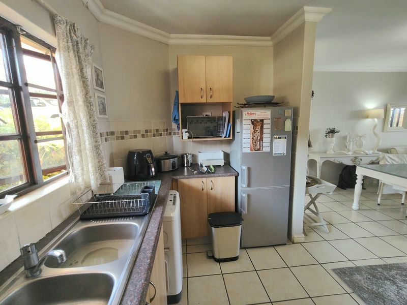 A functional kitchen area featuring laminate countertops, double bowl stainless steel sink, tiled backsplash, and built-in cabinetry, flowing into the adjacent living space.
