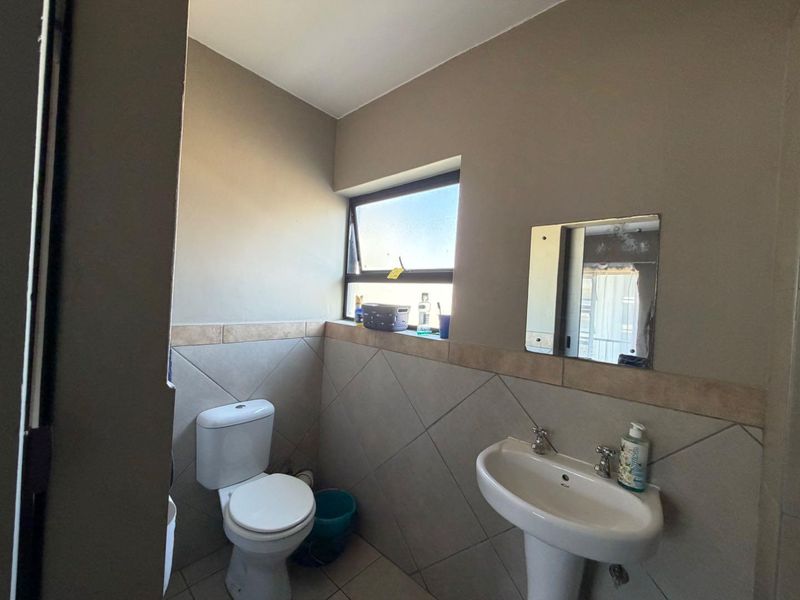 A functional bathroom featuring a pedestal basin, toilet, and tiled splashback with a top-hung window for natural ventilation.