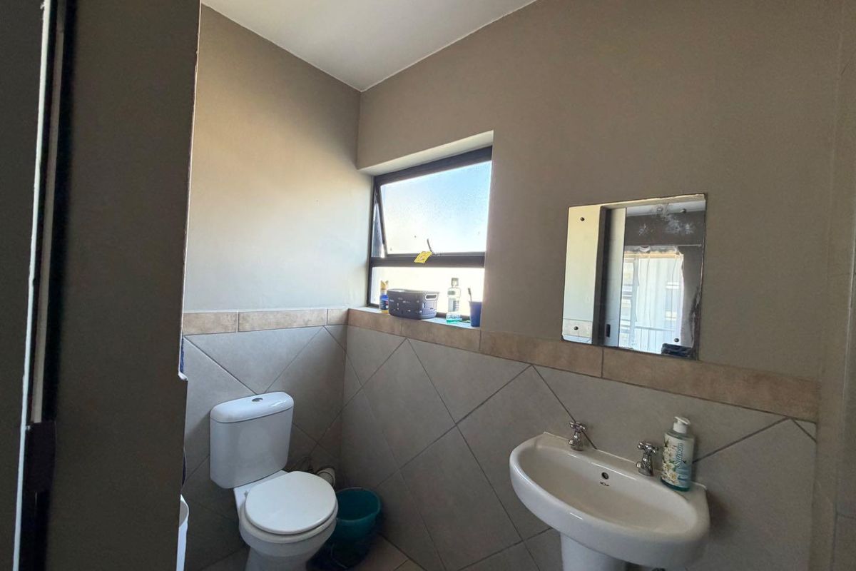 A functional bathroom featuring a pedestal basin, toilet, and tiled splashback with a top-hung window for natural ventilation.
