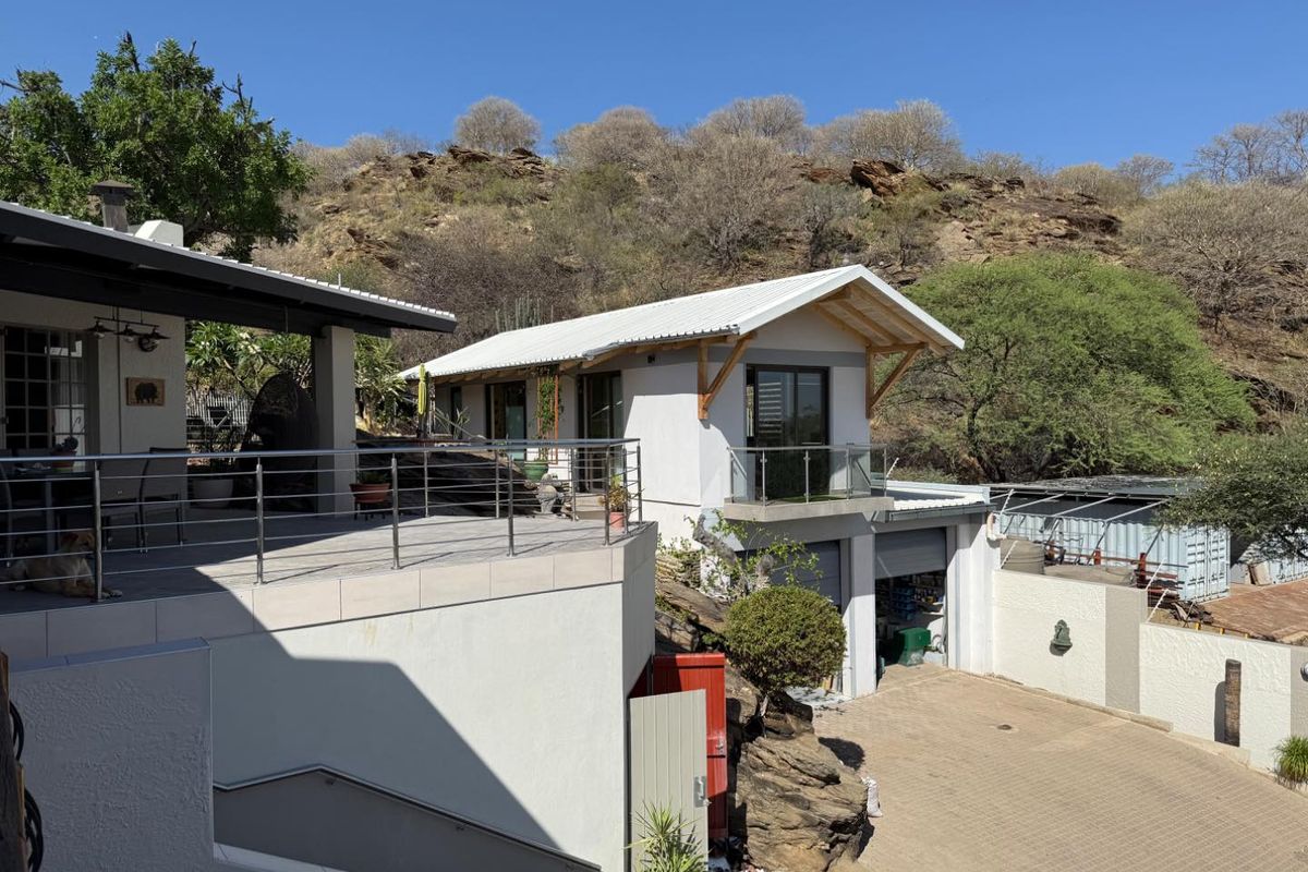 A multi-level residential property featuring a spacious elevated patio with stainless steel railings, a modern white facade, and a paved driveway area.