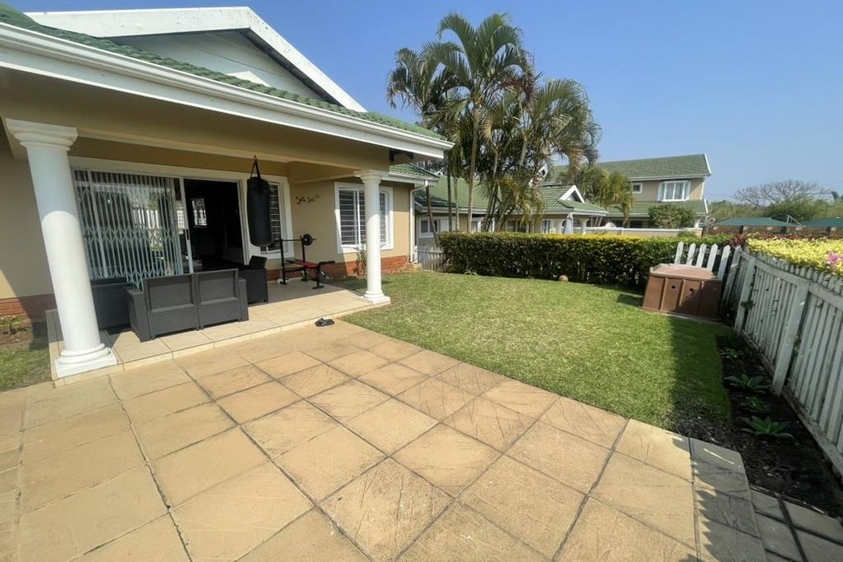 Rear view of the townhouse featuring a covered patio with tiled flooring, a private lawn area, and established garden hedging.