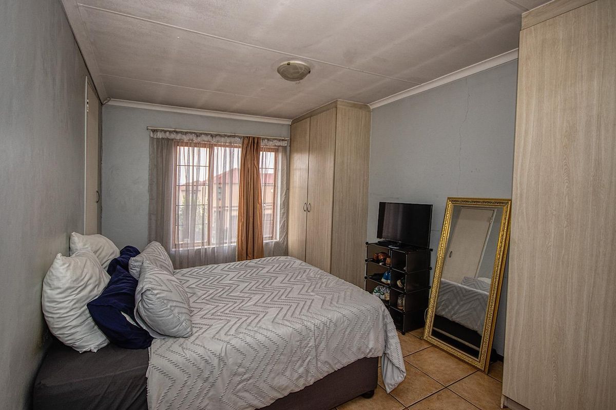 A functional bedroom featuring built-in wooden cupboards, tiled flooring, and natural light through a standard window.