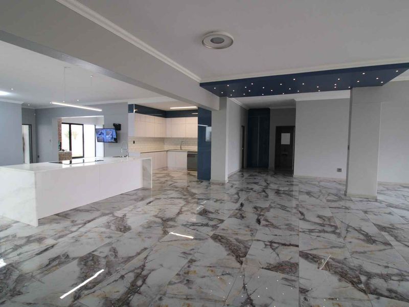 Spacious open-plan living and kitchen area featuring high-end marble-look floor tiles, a central kitchen island, and a modern decorative bulkhead ceiling.