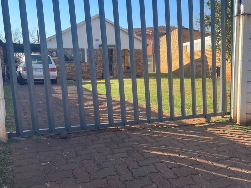 Front view of a residential property featuring a paved driveway, a well-maintained lawn, and a secure metal perimeter gate.