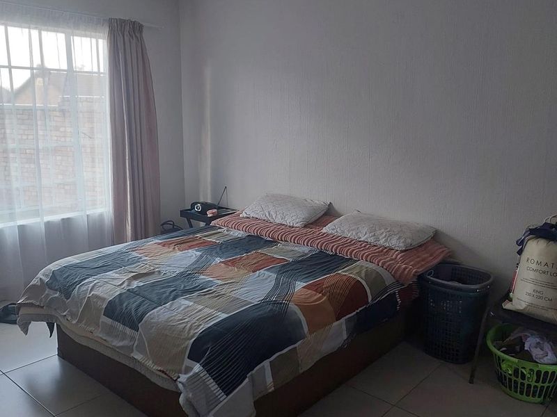 A standard bedroom featuring tiled flooring and a window with security bars, providing a functional space with neutral wall finishes.