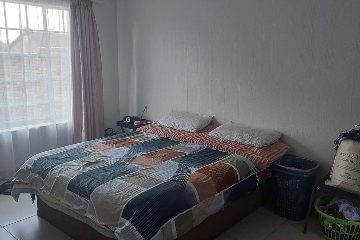A standard bedroom featuring tiled flooring and a window with security bars, providing a functional space with neutral wall finishes.