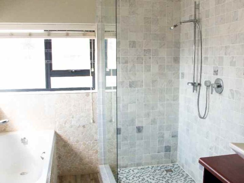 Modern bathroom featuring a walk-in shower with glass screen, built-in bathtub, mosaic floor tiling, and an exposed timber ceiling beam.
