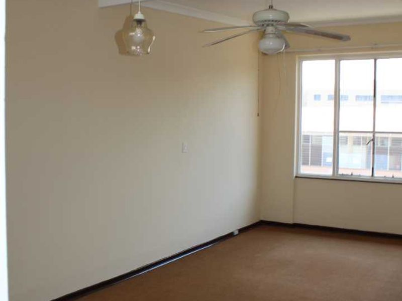 An empty living room featuring carpet flooring, a ceiling fan, and a pendant light, offering a blank canvas for personalization.