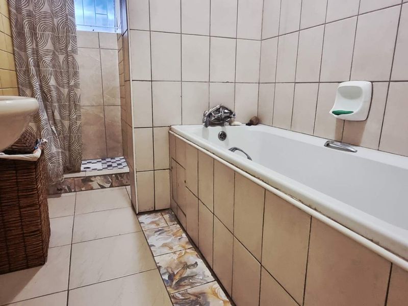 A functional bathroom featuring a bathtub, separate shower area, and pedestal basin with neutral ceramic wall and floor tiling.