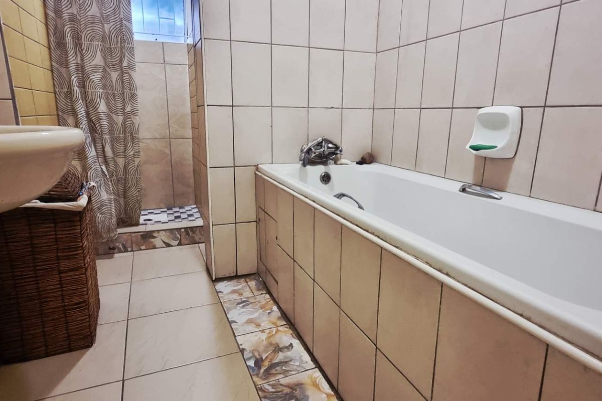 A functional bathroom featuring a bathtub, separate shower area, and pedestal basin with neutral ceramic wall and floor tiling.
