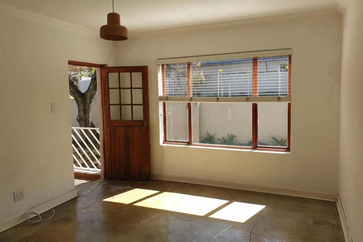 A bright, empty living room featuring polished concrete floors, a wooden door leading to an outdoor area, and large windows with fitted blinds.