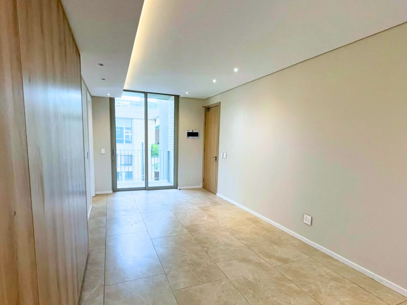 A bright, modern, and empty living area featuring neutral tiled flooring, recessed cove lighting, and a sliding glass door leading to a balcony.