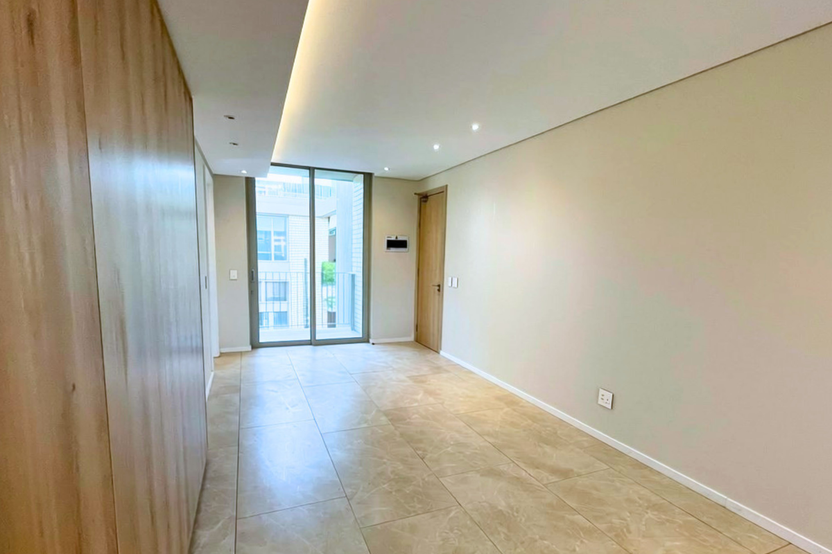 A bright, modern, and empty living area featuring neutral tiled flooring, recessed cove lighting, and a sliding glass door leading to a balcony.