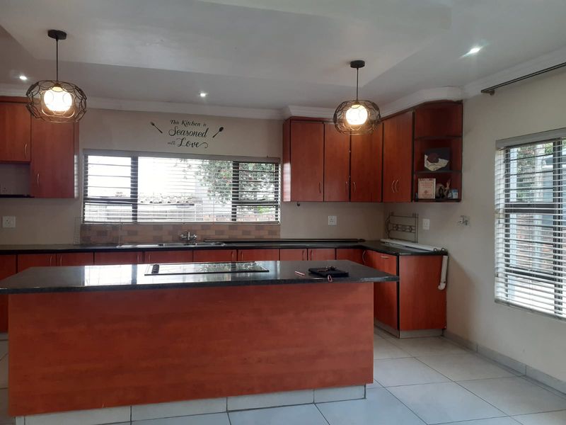 Spacious kitchen featuring warm-toned wooden cabinetry, granite countertops, a central island with a built-in cooktop, and ample natural light from large windows.
