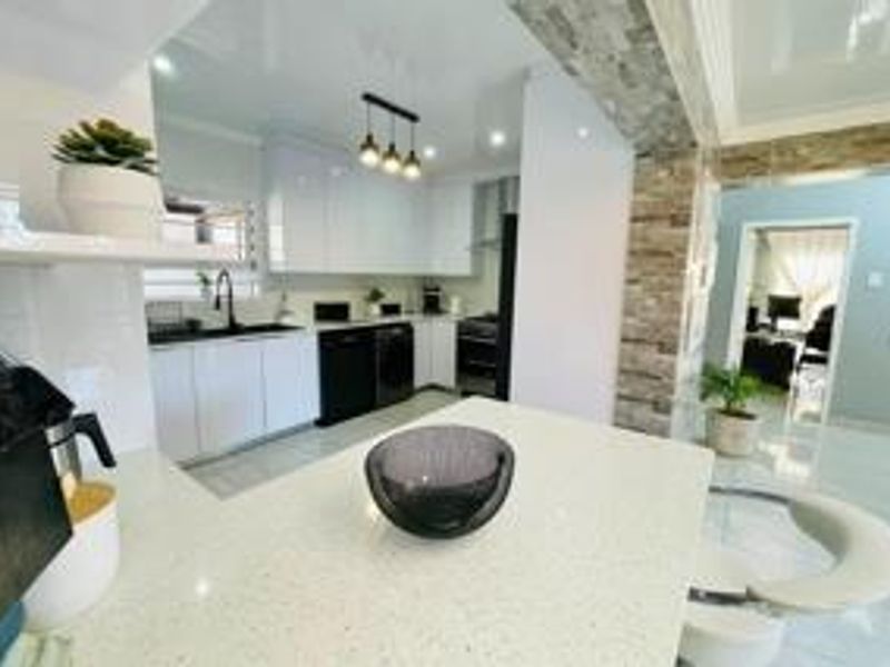 Modern open-plan kitchen featuring sleek gloss cabinetry, quartz countertops, and a stone-clad feature wall, seamlessly flowing into the adjacent living area.
