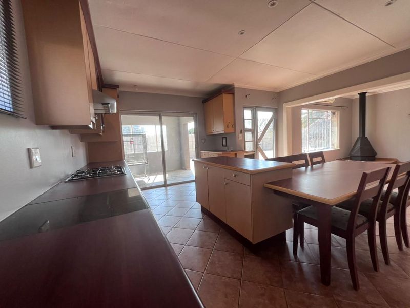 Open-plan kitchen and dining area featuring built-in cabinetry, a gas hob, kitchen island, and a cozy freestanding fireplace with tiled flooring throughout.