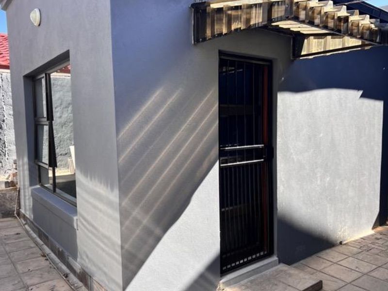 Rear exterior view of the cottage featuring a secure entrance with a metal security gate, protective awning, and paved patio area.