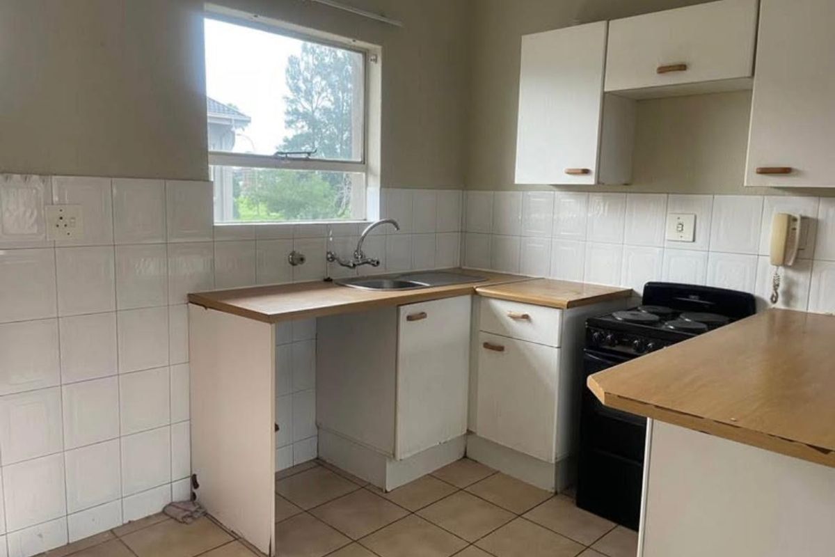 A functional kitchen featuring white cabinetry, tiled splashbacks, a stainless steel sink, and space for a freestanding stove.