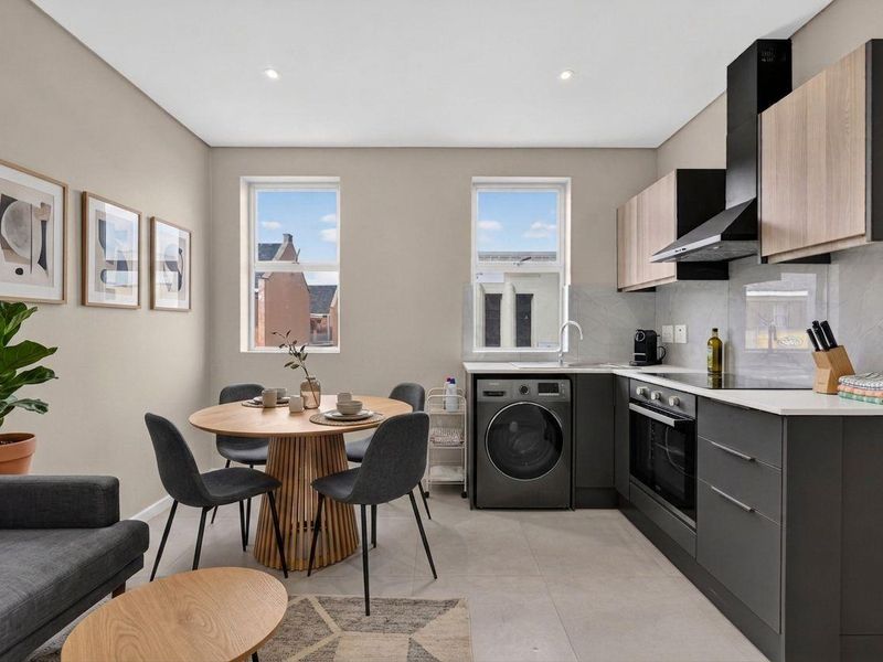Modern open-plan kitchen and dining area featuring sleek cabinetry, integrated appliances, tiled flooring, and ample natural light from dual windows.