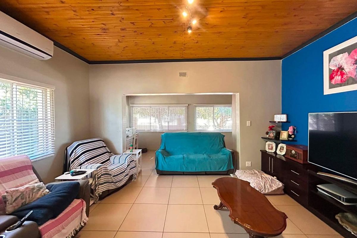 Spacious living room featuring a warm timber tongue and groove ceiling, tiled flooring, and a split system air conditioner for climate control.