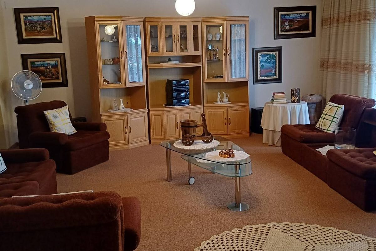 A spacious living room featuring carpeted flooring, an arched entryway leading to an adjacent room, and large windows with curtains.