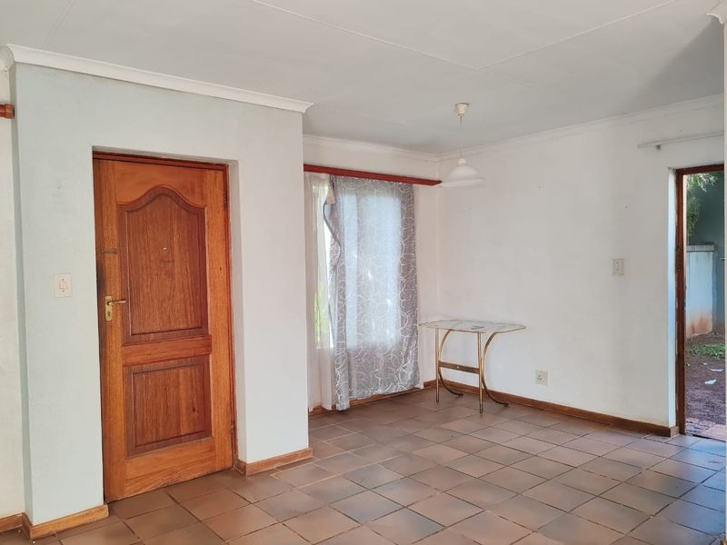 A vacant living area featuring tiled flooring, a solid wooden door, and simple pendant lighting, offering a blank canvas for renovation or interior design.