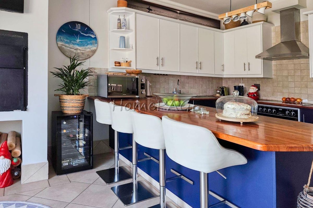 A functional kitchen featuring a wooden breakfast bar, white cabinetry, tiled backsplash, and a stainless steel extractor fan.