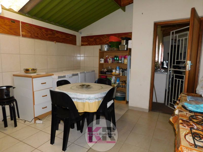 A functional kitchen area featuring tiled flooring, tiled splashbacks, and an exposed timber roof structure, with a security gate leading to an adjacent space.