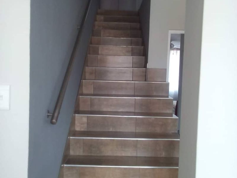 A clean, tiled staircase with a handrail leading to an upper level, featuring modern grey wall accents.
