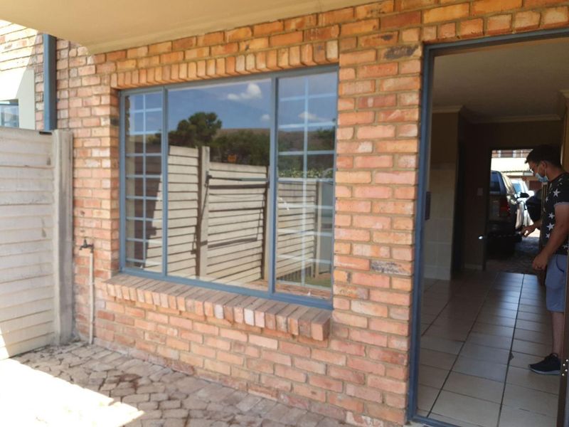 Rear exterior view of the townhouse featuring face brick construction, security bars on windows, and a paved patio area.