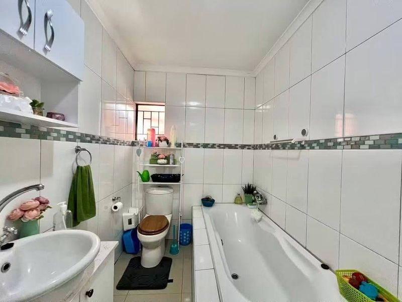 A functional bathroom featuring white wall tiles with a decorative mosaic border, a built-in vanity, a bathtub, and a standard toilet.