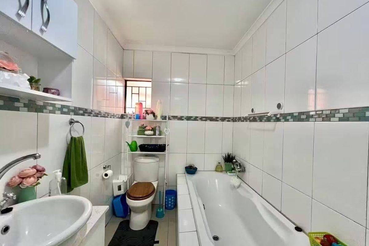 A functional bathroom featuring white wall tiles with a decorative mosaic border, a built-in vanity, a bathtub, and a standard toilet.