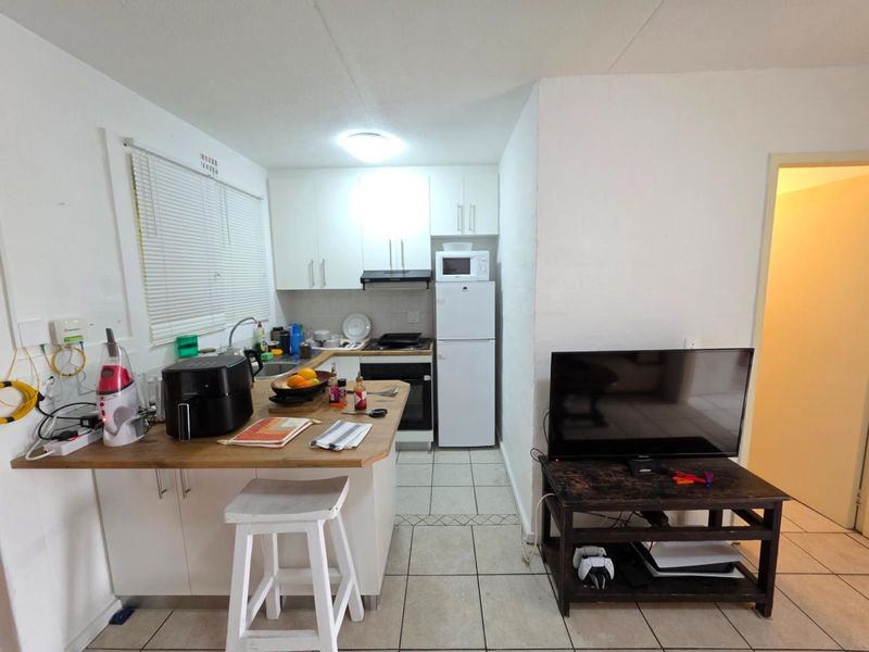 Compact open-plan kitchen featuring white cabinetry, built-in oven, extractor fan, and tiled flooring, seamlessly integrated with the living area.