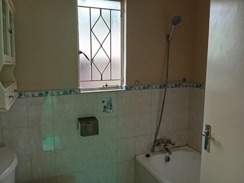 A functional bathroom featuring a bathtub with a handheld shower attachment, tiled walls, and a window with security bars.